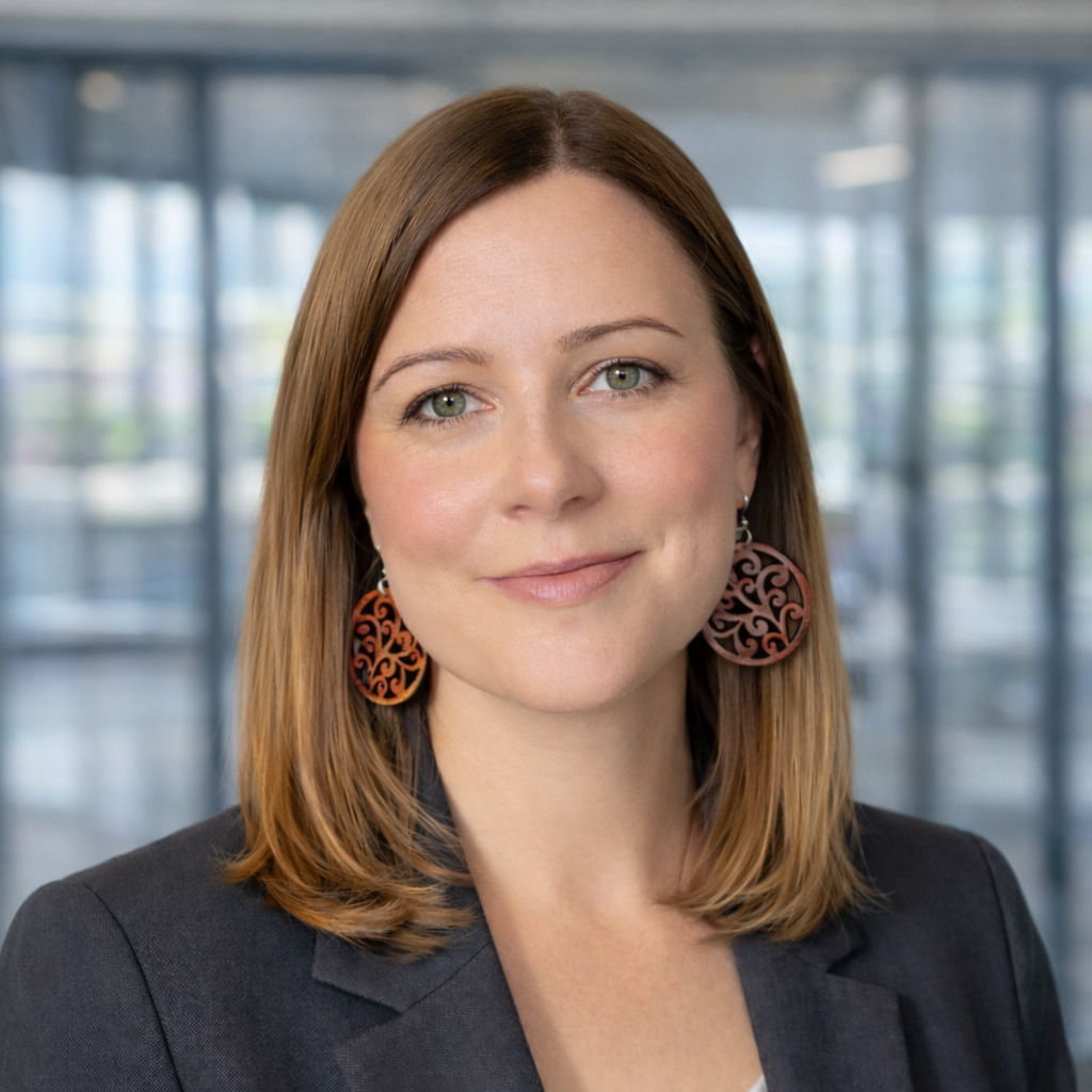 Professional headshot of a woman with shoulder-length reddish-brown hair wearing a dark blazer and decorative copper-toned