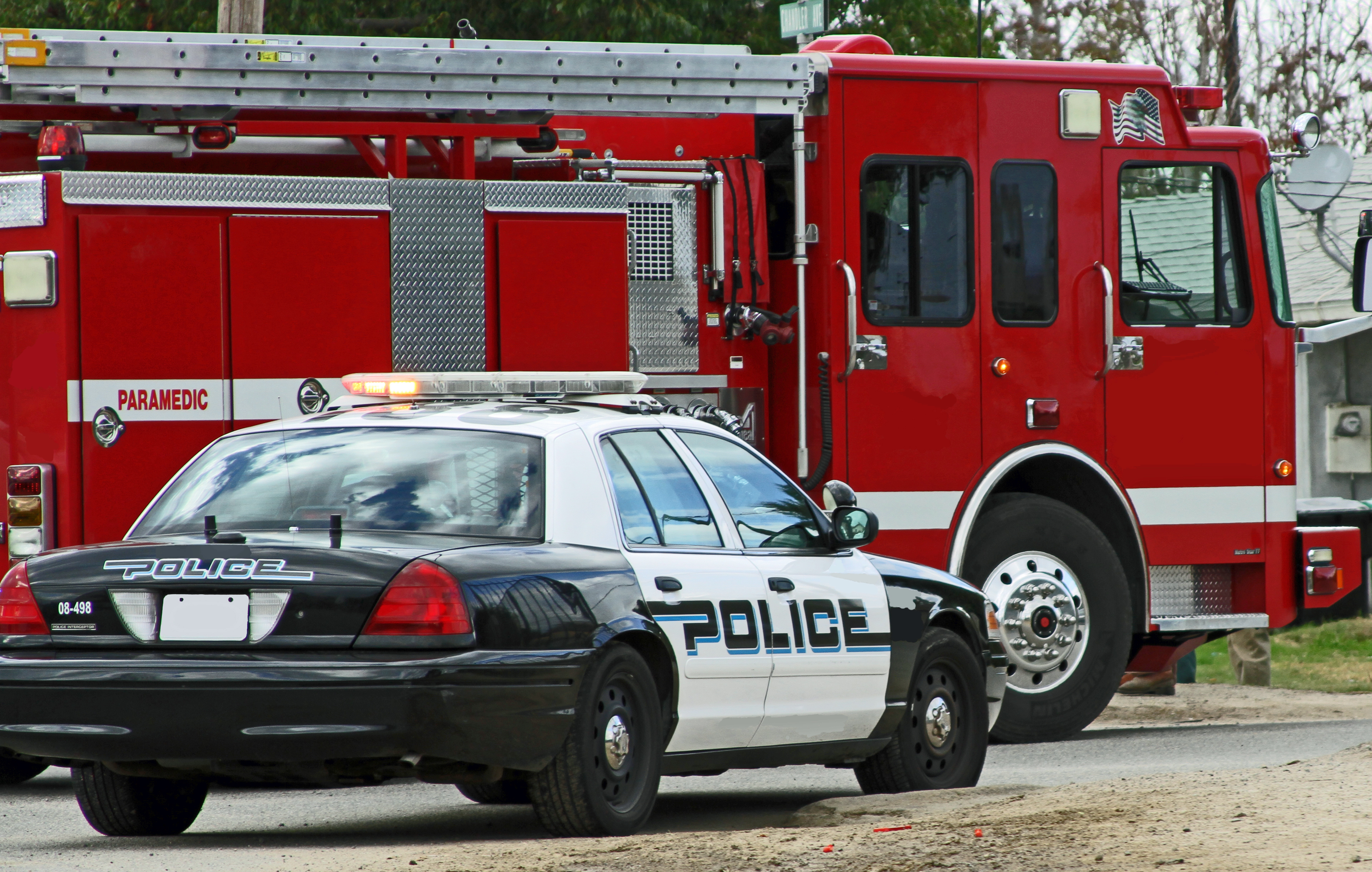 Black and white police car parked in front of red fire truck with extended ladder