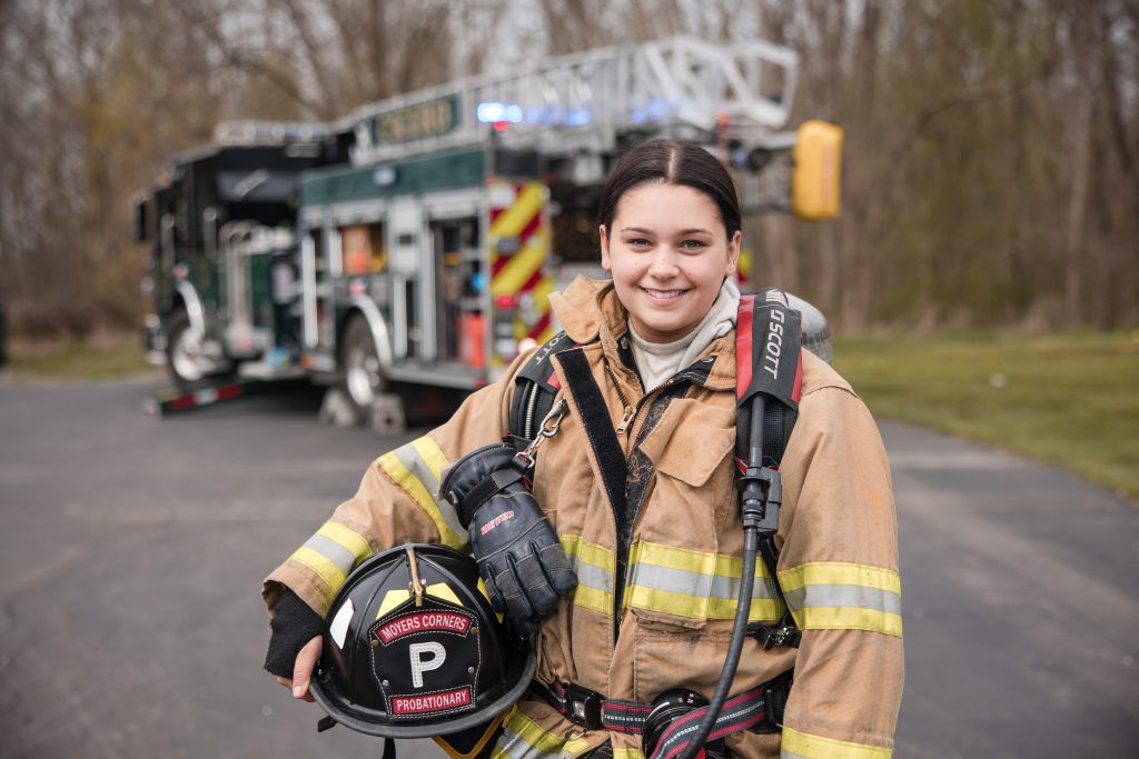 A smiling firefighter in full gear holding a helmet